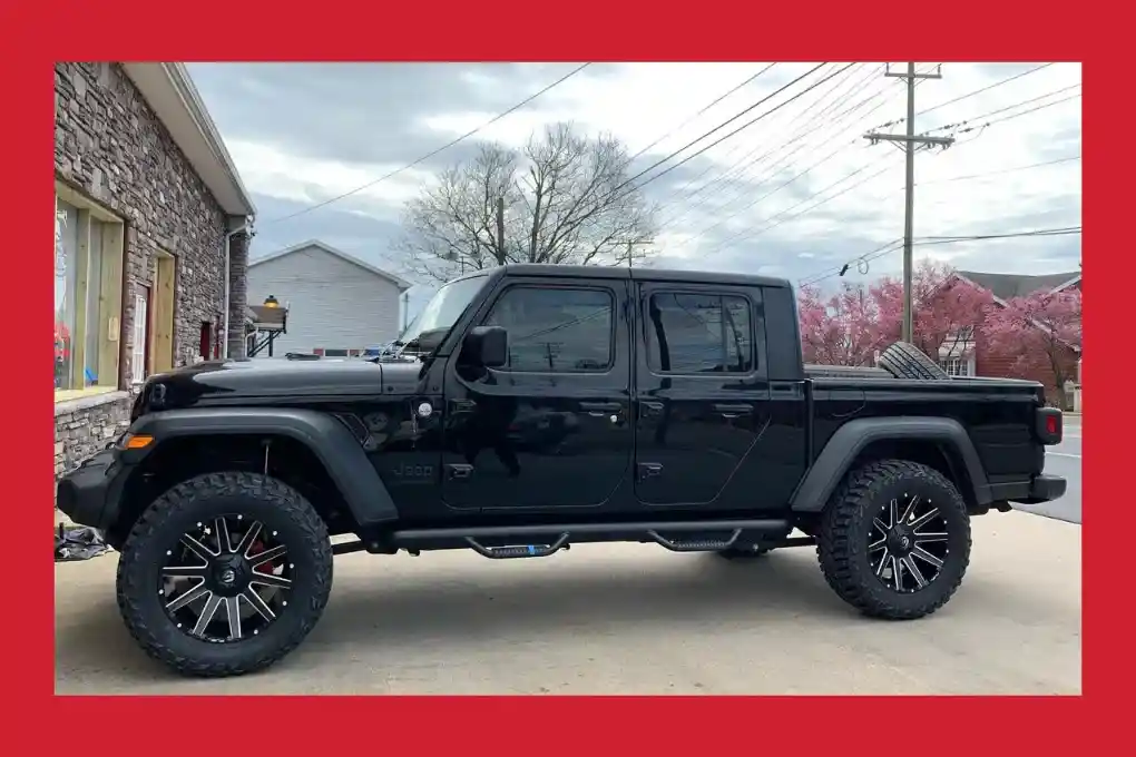 A black jeep equipped with a large front tire, emphasizing its robust appearance and suitability for adventurous terrains.