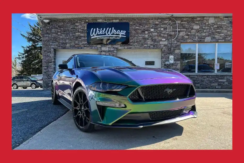 A striking purple Mustang is parked in front of a contemporary building, highlighting its unique color and design.