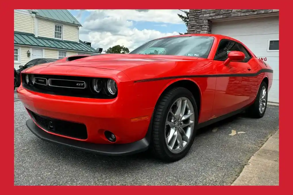 A red Dodge Challenger parked in front of a residential house, showcasing its sleek design and vibrant color.